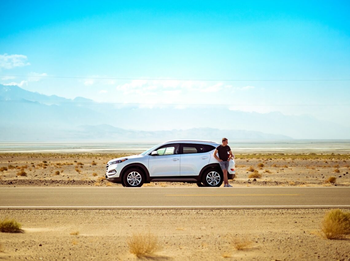 man standing beside white SUV near concrete road under blue sky at daytime