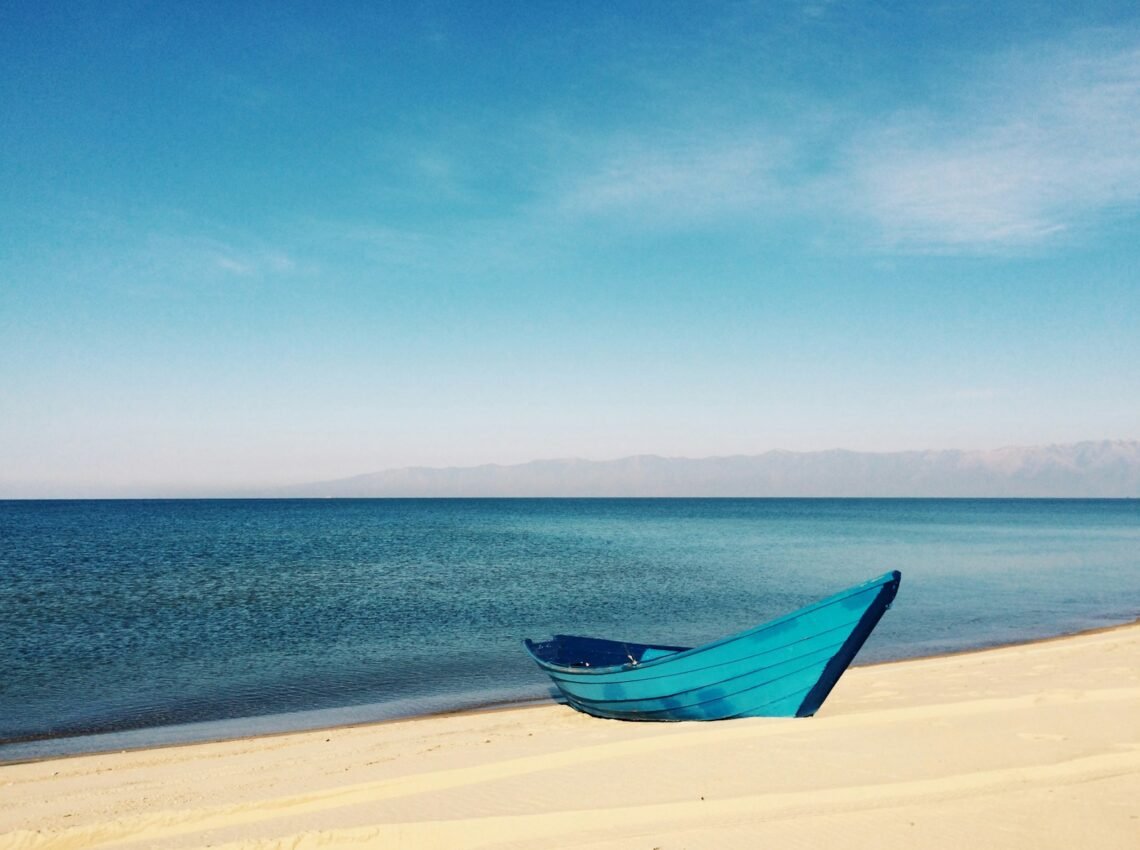 blue boat on sand near body of water during daytime